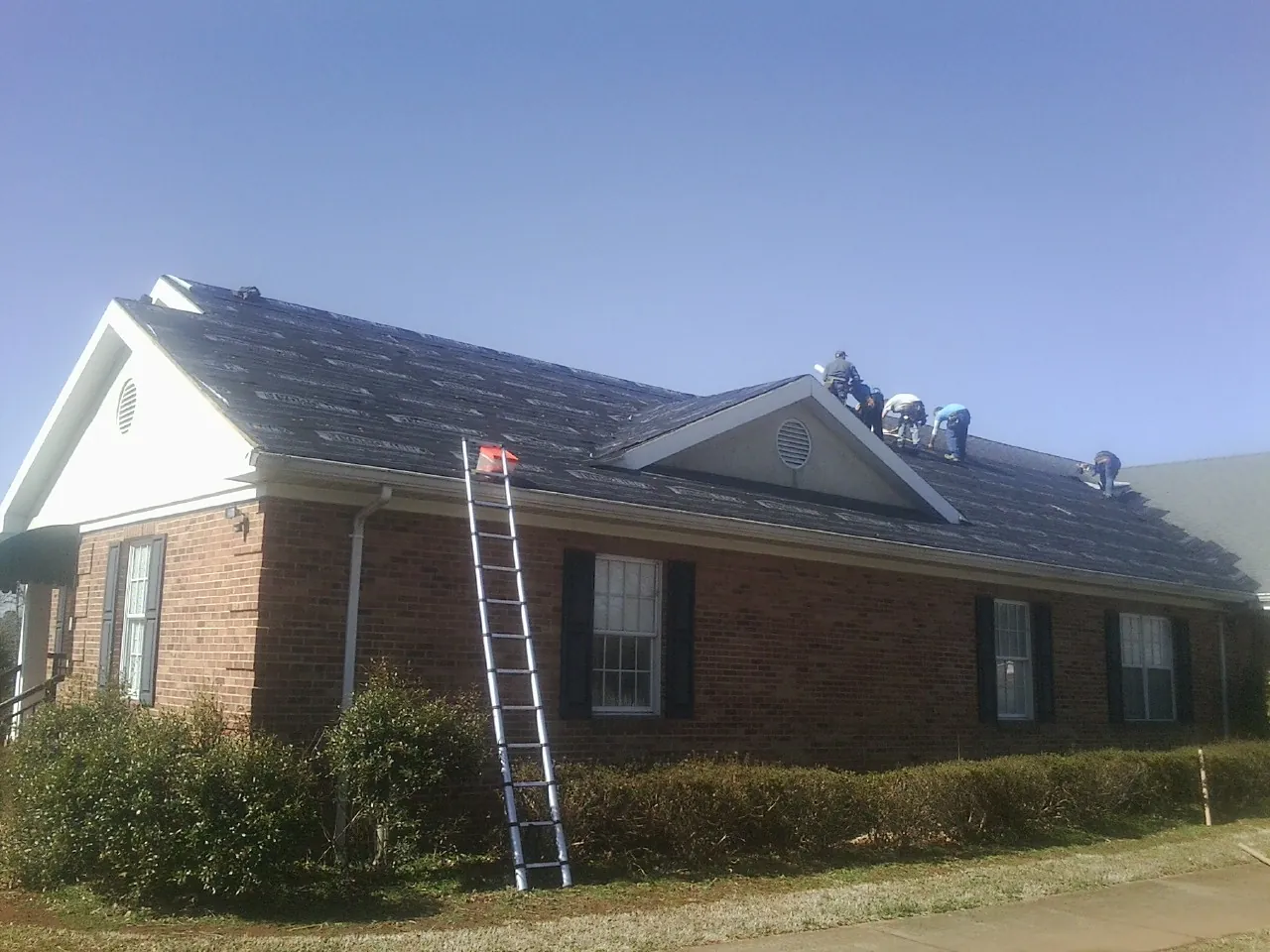 Crew tearing shingles off a brick ranch roof with a ladder set — Emergency Roof Repair work by our crew in Minneapolis
