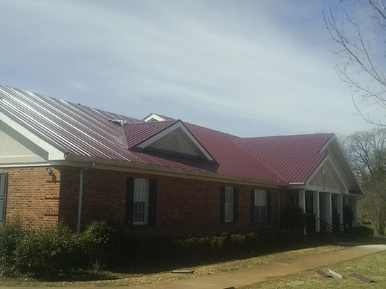 Red metal roof with gabled entries on a long brick building, from a Hail Damage Roof Repair job in Minneapolis
